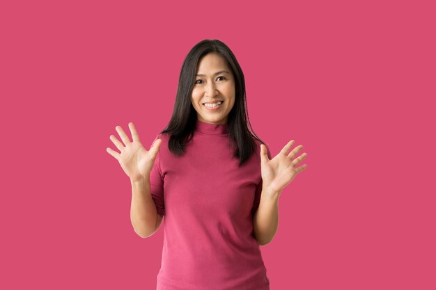 Une femme asiatique heureuse lève les paumes de joie, heureuse de recevoir isolée sur fond rose