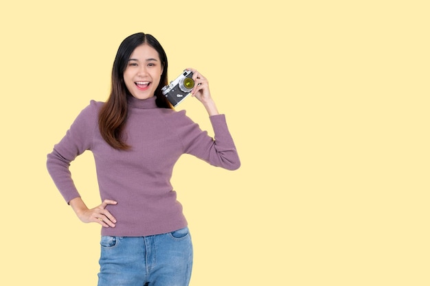 Une femme asiatique heureuse tient son appareil photo argentique vintage debout sur un fond jaune isolé