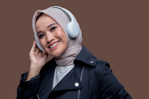 Femme asiatique de hijab portant des écouteurs sans fil avec un sourire regardant la caméra