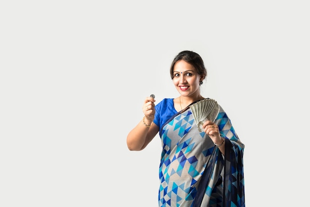 Femme asiatique indienne en sari ou sari montrant ou tenant des billets de banque en papier ou un ventilateur d'argent contre un mur blanc
