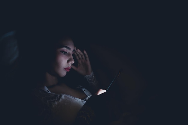 Femme asiatique jouant à un jeu sur smartphone dans le lit la nuitThailand peopleAddict social media