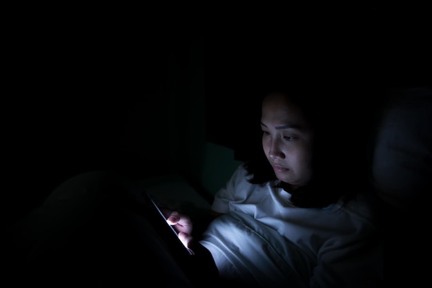 Femme asiatique jouant à un jeu sur smartphone dans le lit la nuitThailand peopleAddict social media