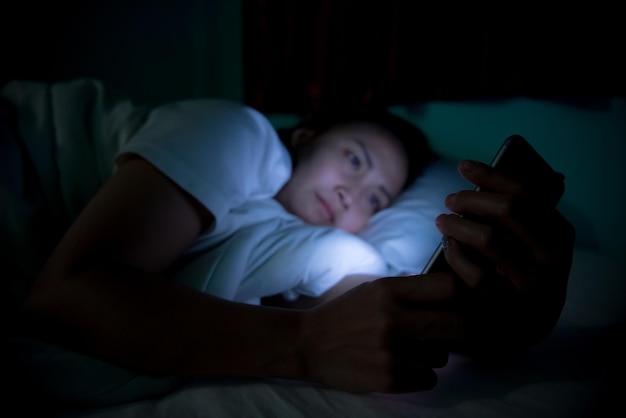 Femme asiatique jouant à un jeu sur smartphone dans le lit la nuitThailand peopleAddict social media