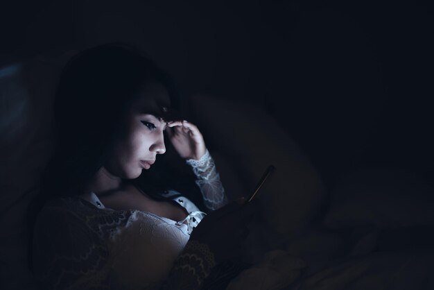 Femme asiatique jouant à un jeu sur smartphone dans le lit la nuitThailand peopleAddict social media