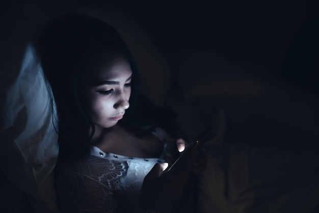 Femme asiatique jouant à un jeu sur smartphone dans le lit la nuitThailand peopleAddict social media