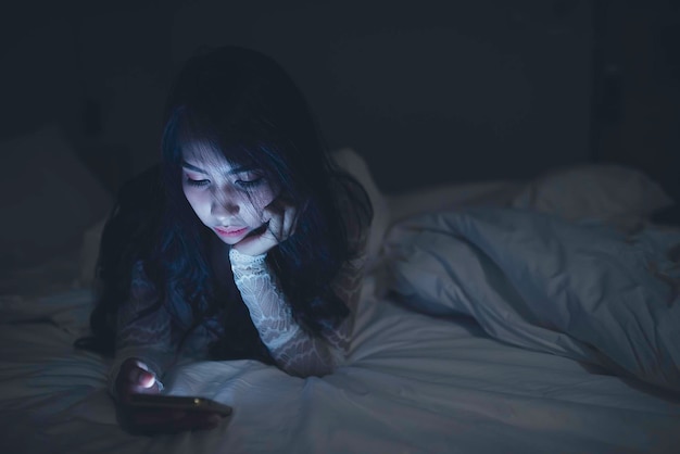 Femme asiatique jouant à un jeu sur smartphone dans le lit la nuitThailand peopleAddict social media