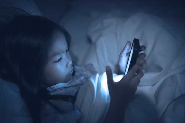 Femme asiatique jouant à un jeu sur smartphone dans le lit la nuitThailand peopleAddict social media