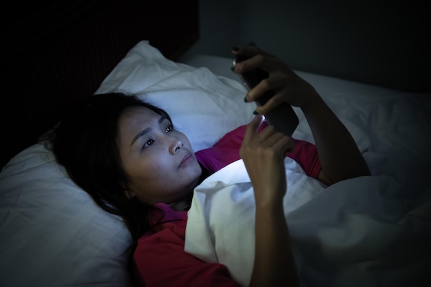 Femme asiatique jouant à un jeu sur smartphone dans le lit la nuitThailand peopleAddict social media