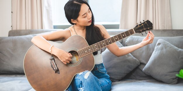 Femme asiatique jouant de la musique à la guitare à la maison, mode de vie d'une jeune musicienne guitariste avec instrument d'art acoustique assis pour jouer et chanter une chanson faisant du son en passe-temps dans la chambre de la maison