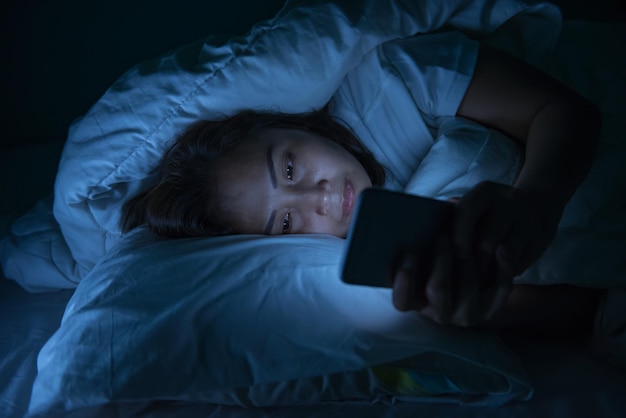 Une femme asiatique joue au smartphone dans le lit la nuitThaïlandais