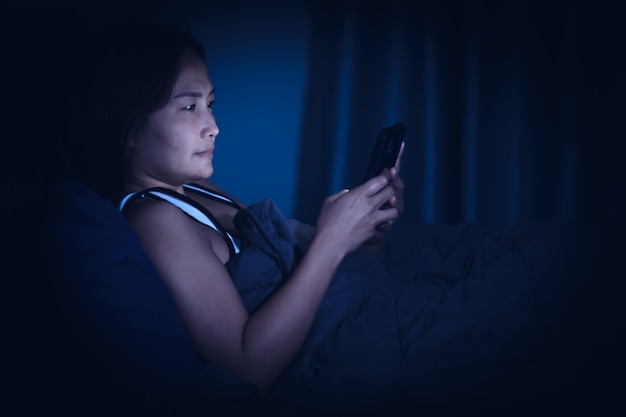 Une femme asiatique joue au smartphone dans le lit la nuitThaïlandais