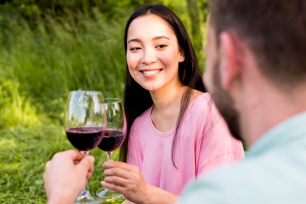 Femme asiatique joyeuse grillage des verres à vin avec son petit ami et souriant