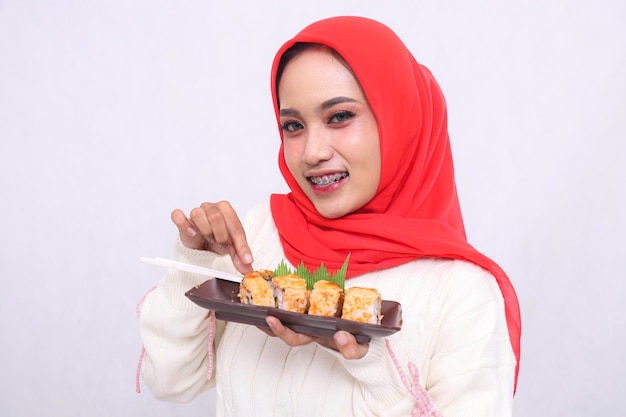 une femme asiatique joyeuse en hijab regardant la caméra faisant des gestes avec ses mains et tenant une assiette
