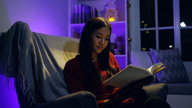 Femme asiatique lisant un livre dans le salon la nuit. Style de vie et détente à la maison.