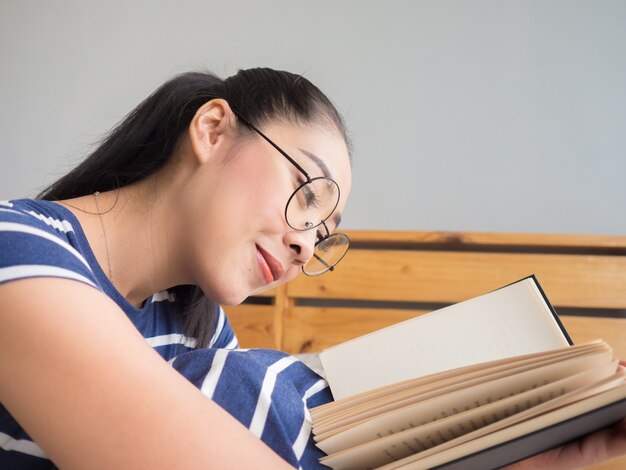 Femme asiatique avec des lunettes lire un livre dans la chambre.