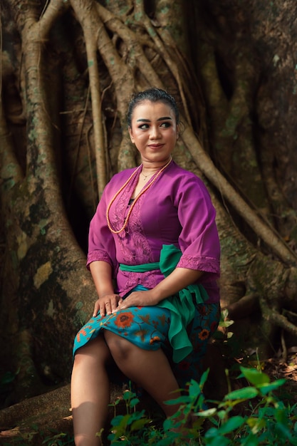 Une femme asiatique magnifiquement assise sur le grand arbre dans une robe violette tout en visitant la jungle