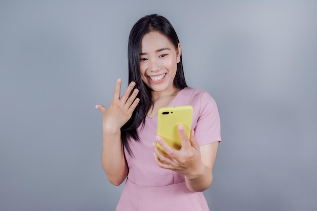 Femme asiatique à la maison faisant un appel vidéo à l'aide d'un téléphone intelligent sur fond gris