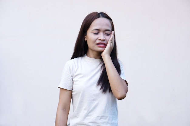 La femme asiatique avec le mal de dents touche la joue avec sa main