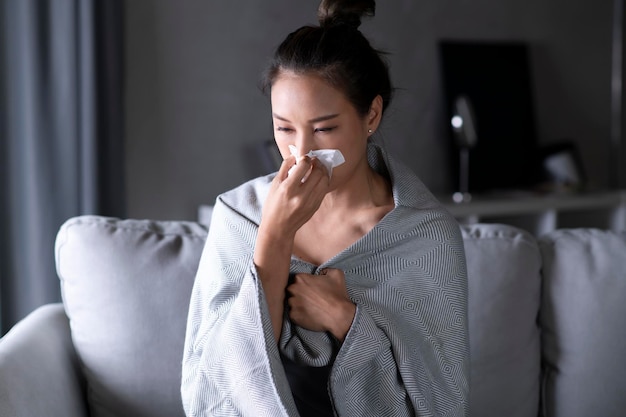 Femme Asiatique Malade Et éternue Avec Du Papier De Soie Sur Le Canapé à La Maison