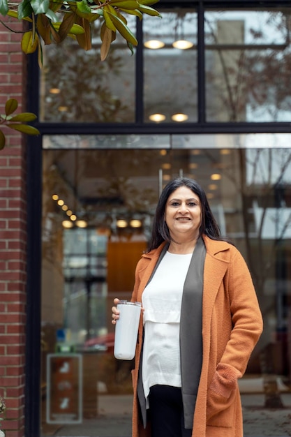 Femme asiatique mature confiante dans des vêtements décontractés souriant caméra debout contre un bâtiment urbain loft