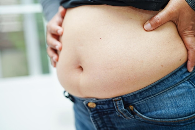 Une femme asiatique montre un gros ventre en surpoids et en obésité au bureau
