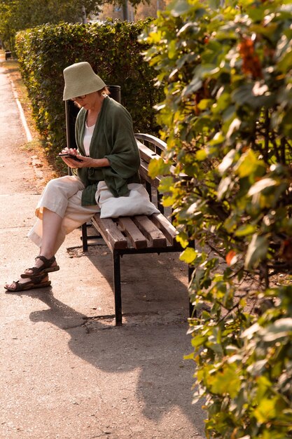 femme asiatique mûre en chapeau et vêtements en lin utilisant un smartphone pour discuter sur les réseaux sociaux