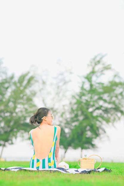 Photo femme asiatique avec panier de pique-nique assis sur une couverture au parc d'été