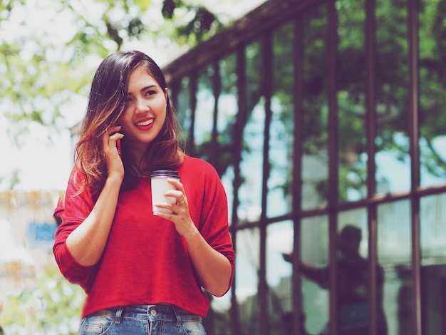 Femme asiatique parlant au téléphone pendant que vous buvez du café à l&#39;extérieur.