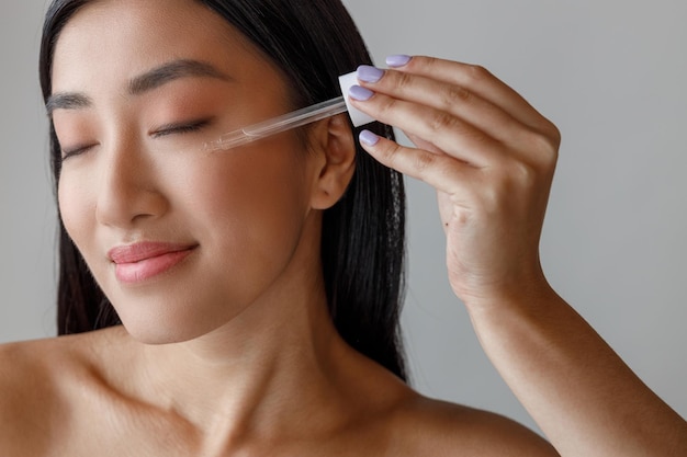 Femme asiatique avec une peau parfaite appliquant du sérum vitaminé sur son visage