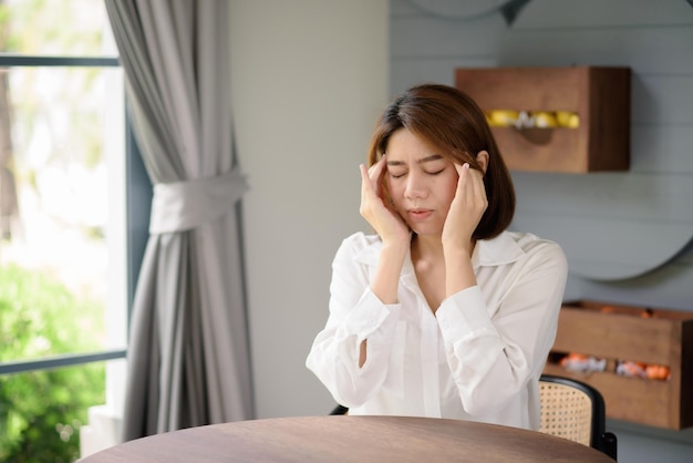 Une femme asiatique place ses mains près de sa tête tout en souffrant d'un mal de tête