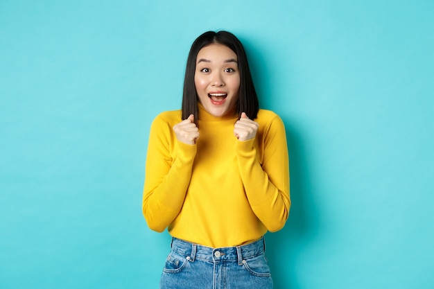 Femme asiatique pleine d'espoir et heureuse regardant avec étonnement et espoir à la caméra, gagnant, debout sur fond bleu.