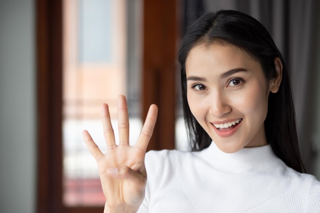 Femme asiatique pointant en comptant quatre doigts portrait d'une femme asiatique souriante heureuse pointant vers le haut 4 doigts pour le concept numéro quatre ou 4 points par le modèle de femme adulte asiatique chinoise thème décontracté intérieur