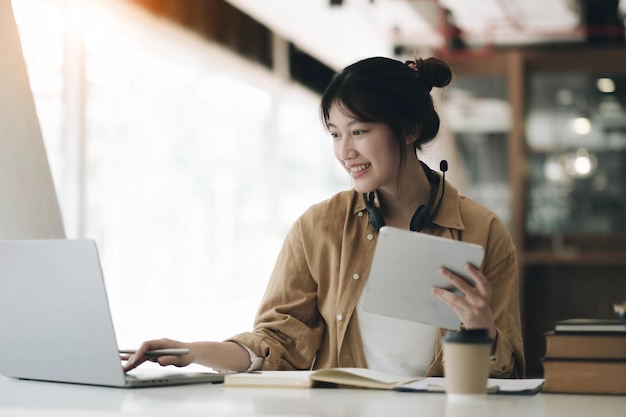 Femme asiatique portant des écouteurs autour du cou à l'aide d'un ordinateur portable et enregistrant les devoirs de l'enseignant