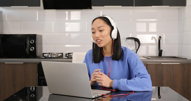 Femme asiatique portant des écouteurs étudiant en ligne depuis la maison en regardant une leçon de cours sur le Web ou en écoutant un tuteur par appel vidéo elearning sur l'isolement pandémique. L'enseignement à distance.