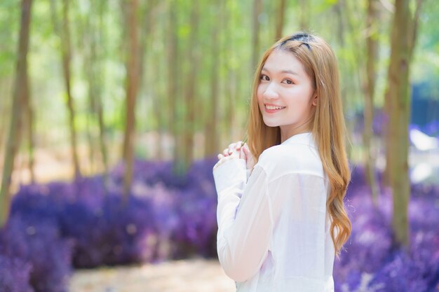 Une femme asiatique portant une longue chemise blanche sourit joyeusement et se tient dans le jardin comme elle est naturelle