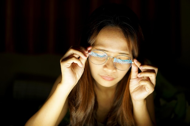 Femme asiatique portant des lunettes Pour voir l'ordinateur en basse lumière, regarder des films en ligne