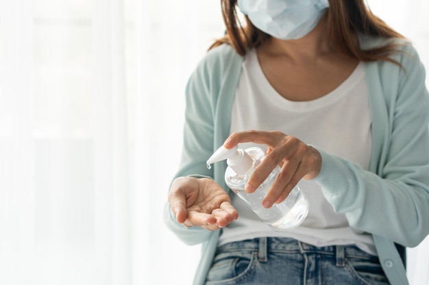 Une femme asiatique portant un masque médical applique un gel antiseptique à l'alcool sur sa main Mesures de protection pour prévenir la transmission de COVID19 et nouveau concept de mode de vie normal Gros plan