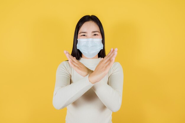 Femme asiatique portant un masque médical pour protéger Covid-19 (Coronavirus), arrêtez de sortir sur fond jaune, la distanciation sociale et la quarantaine sont importantes