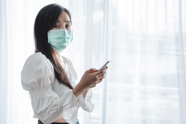 Photo femme asiatique portant un masque protecteur et à l'aide de smartphone mobile