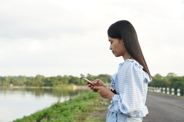 Une femme asiatique portant une robe bleue utilise un fond de nature de téléphone portable