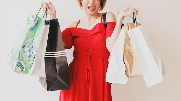 Femme asiatique portant une robe rouge tenant des sacs à provisions avec une expression souriante