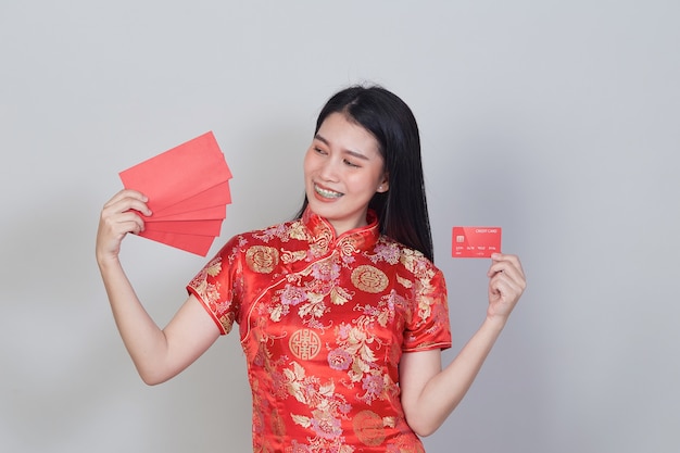 Femme asiatique portant une robe traditionnelle cheongsam qipao montrant une carte de crédit et des enveloppes rouges pour les concepts de shopping du nouvel an chinois.