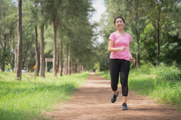 Femme asiatique portant des vêtements de sport roses courant dans le parc pour perdre du poids et rester en bonne santé