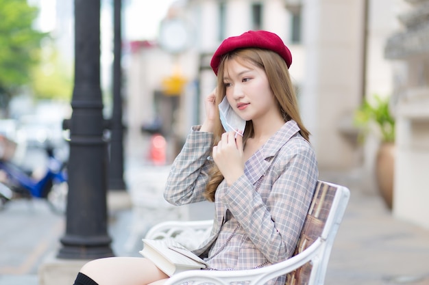 Une femme asiatique porte un costume et une casquette rouge et s'assoit sur un banc tout en portant un masque médical