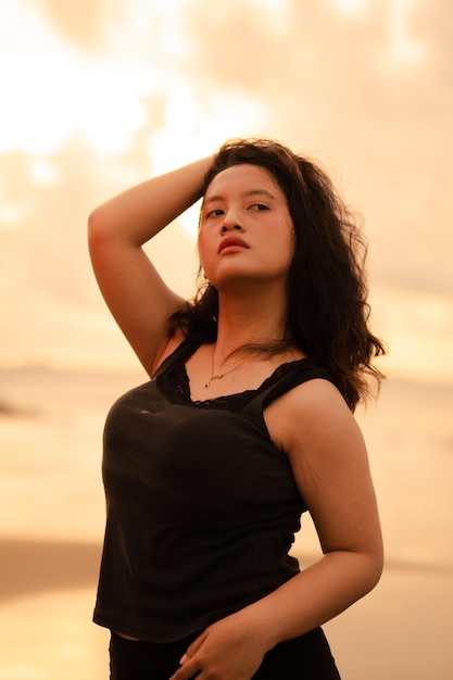 Une femme asiatique posant avec ses mains levées et touchant passionnément ses cheveux noirs sur la plage