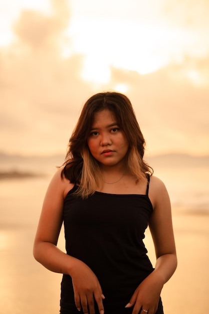 Une femme asiatique pose avec une expression sale et en colère lorsqu'elle porte une robe noire sur la plage