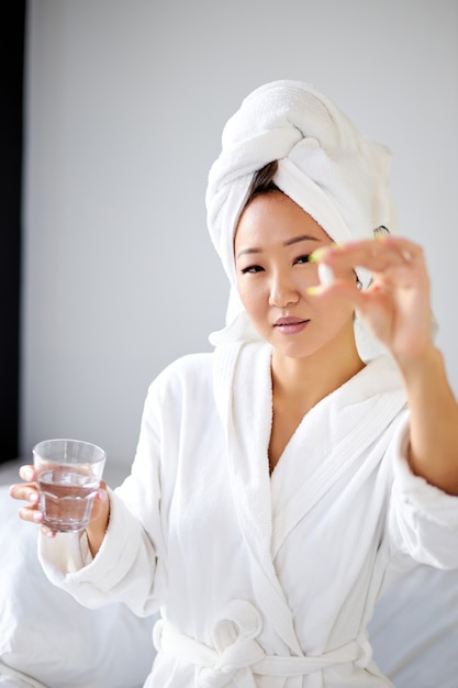 Femme asiatique prenant des médicaments après le réveil le matin, femme en peignoir et serviette ont des médicaments analgésiques souffrent de nausées matinales ou de maux de tête