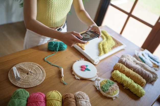 Femme asiatique prenant une photo de smartphone Punch aiguille téléphone affichage sur les réseaux sociaux en studio atelier designer lieu de travail projet d'artisanat fait à la main broderie bricolage