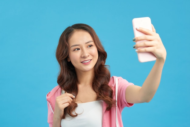 Femme asiatique prenant selfie au smartphone isolé sur fond bleu