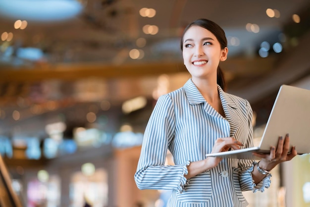 Femme asiatique propriétaire d'entreprise communication à la main avec la technologie d'entreprise smartphone et ordinateur portable avec arrière-plan flou bokeh magasin de deaprtment